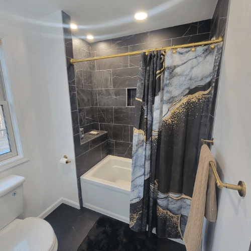 Bathroom shower renovation with black marble tile and gold-accent fixtures by Homes by Covenant`