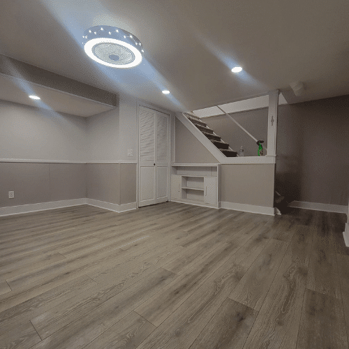 Basement remodel completed with flooring, wall paneling, and ceiling lighting by Homes by Covenant