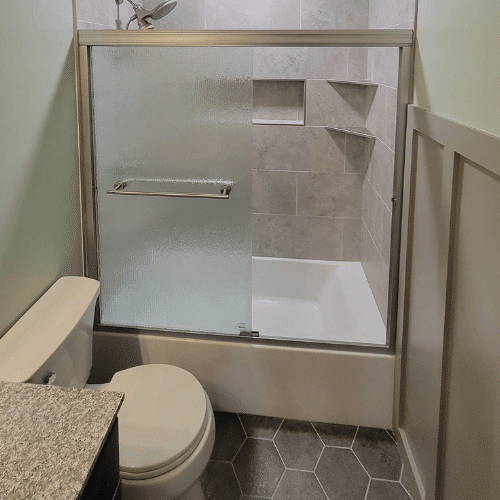 Modern bathroom remodel with gray tile walls, glass shower door, and chrome fixtures by Homes by Covenant