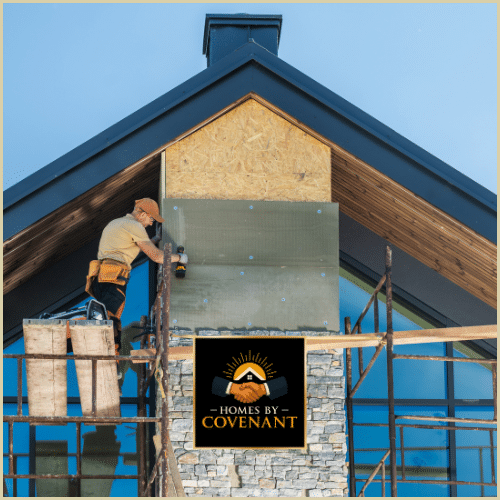 Construction worker installing exterior sheathing on a new home’s gable roof using scaffolding on a clear day.