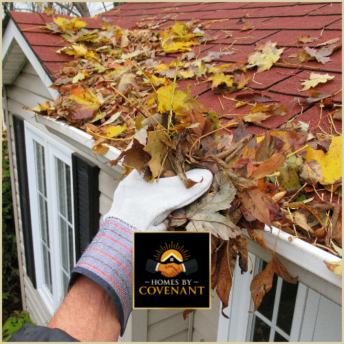 Homeowner removing leaves from a cluttered gutter filled with fall debris.