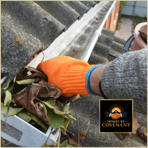 Cleaning wet, packed leaves from a residential gutter using protective gloves.