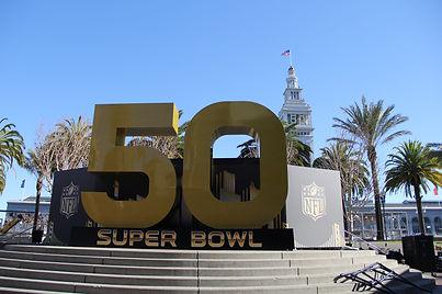 Outdoor landmark featuring the gold “50” sculpture and NFL shield set against a waterfront backdrop.