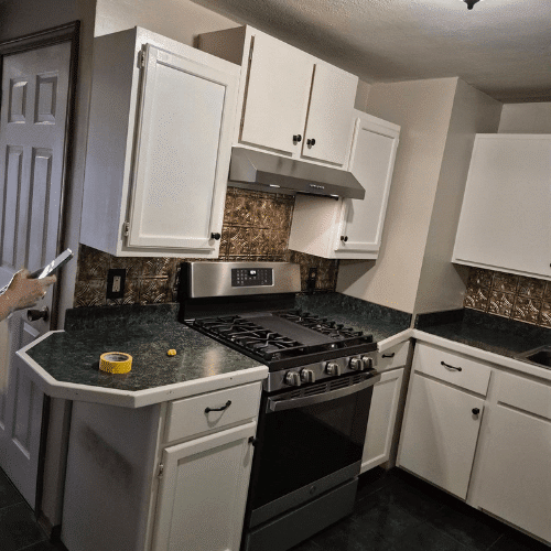 Pre-renovation kitchen before Homes by Covenant remodel, showing white cabinets, dark green countertops, and older backsplash.
